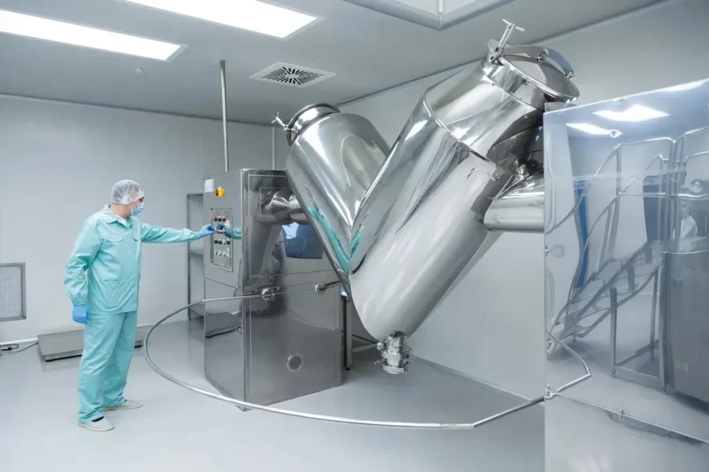 Técnico operando una gran licuadora en V de acero inoxidable en una sala limpia de un laboratorio farmacéutico